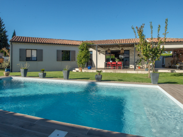 Single-story house with a terracotta tile roof, covered patio, and a large rectangular pool in the foreground.