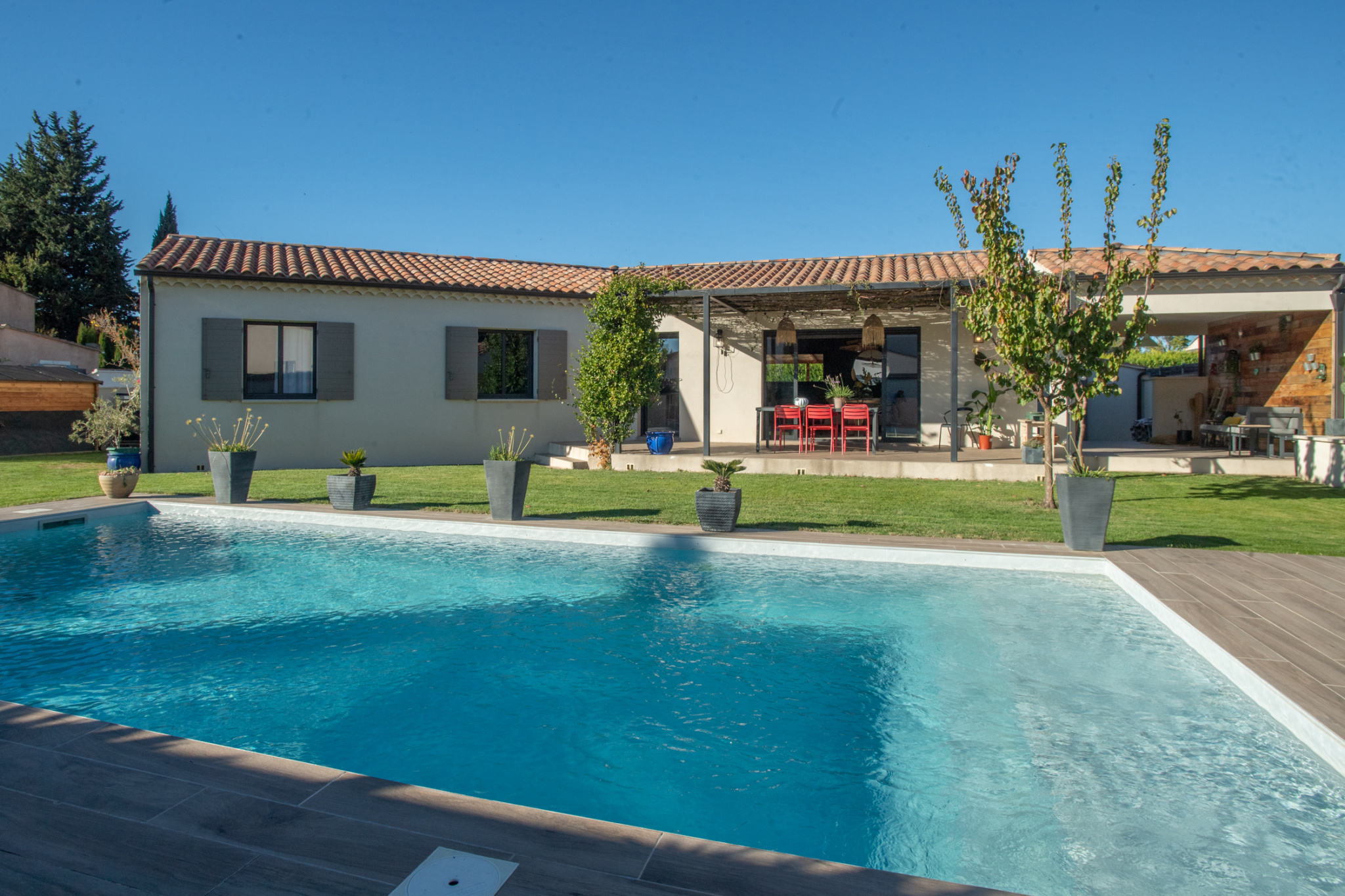 Single-story house with a terracotta tile roof, covered patio, and a large rectangular pool in the foreground.