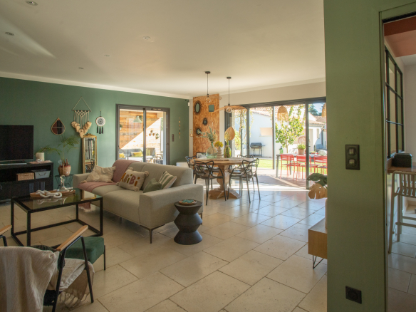 Open-plan living room with a green accent wall, beige sofa, TV cabinet, and a dining area near glass doors.