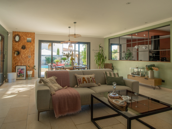 Bright living room with a beige sofa, pink throw, and glass coffee table, open to the dining area and garden patio beyond.