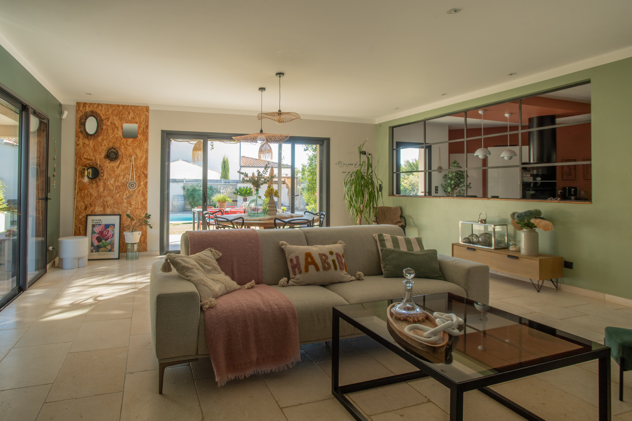 Bright living room with a beige sofa, pink throw, and glass coffee table, open to the dining area and garden patio beyond.