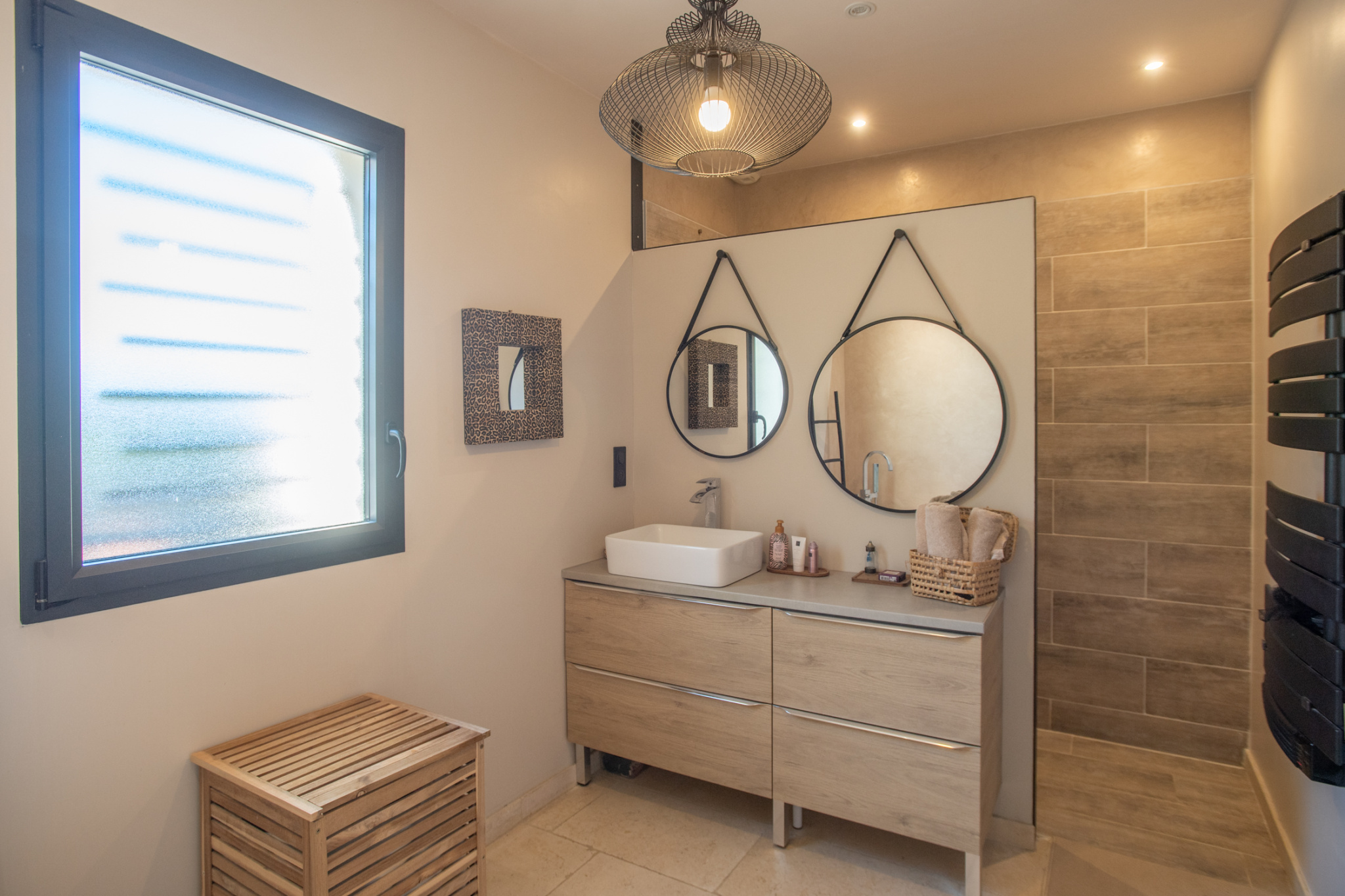 Bathroom with a white vessel sink on a light wood vanity, two round hanging mirrors, and a frosted window to the left.