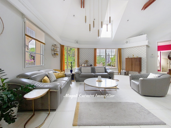 Bright, open living room with grey sectional sofas, a round marble coffee table, and mustard-yellow curtains by large windows letting in natural light.