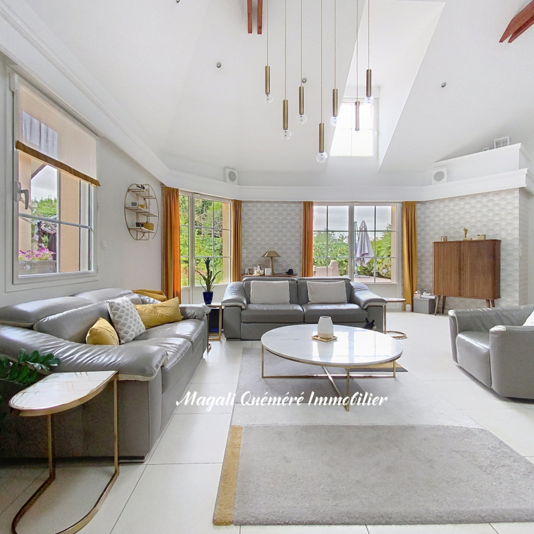 Bright, open living room with grey sectional sofas, a round marble coffee table, and mustard-yellow curtains by large windows letting in natural light.