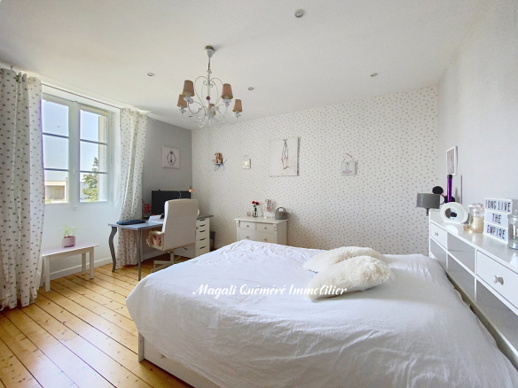 Bright bedroom with a white bed, chandelier, and large window with star-pattern curtains; pale walls and light wood floor.
