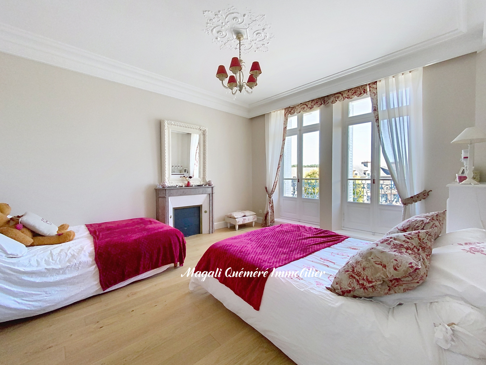 Bright bedroom with two white beds and magenta throws, a chandelier, and tall French windows with sheer curtains