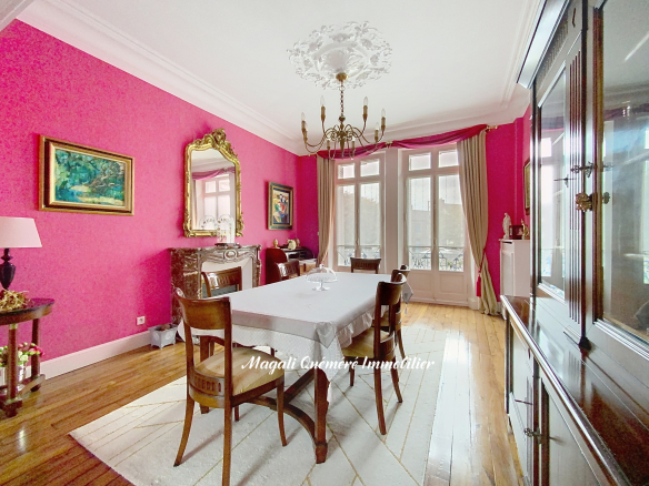 Elegant dining room with pink walls, a long white-covered table, and dark wooden chairs under a chandelier.