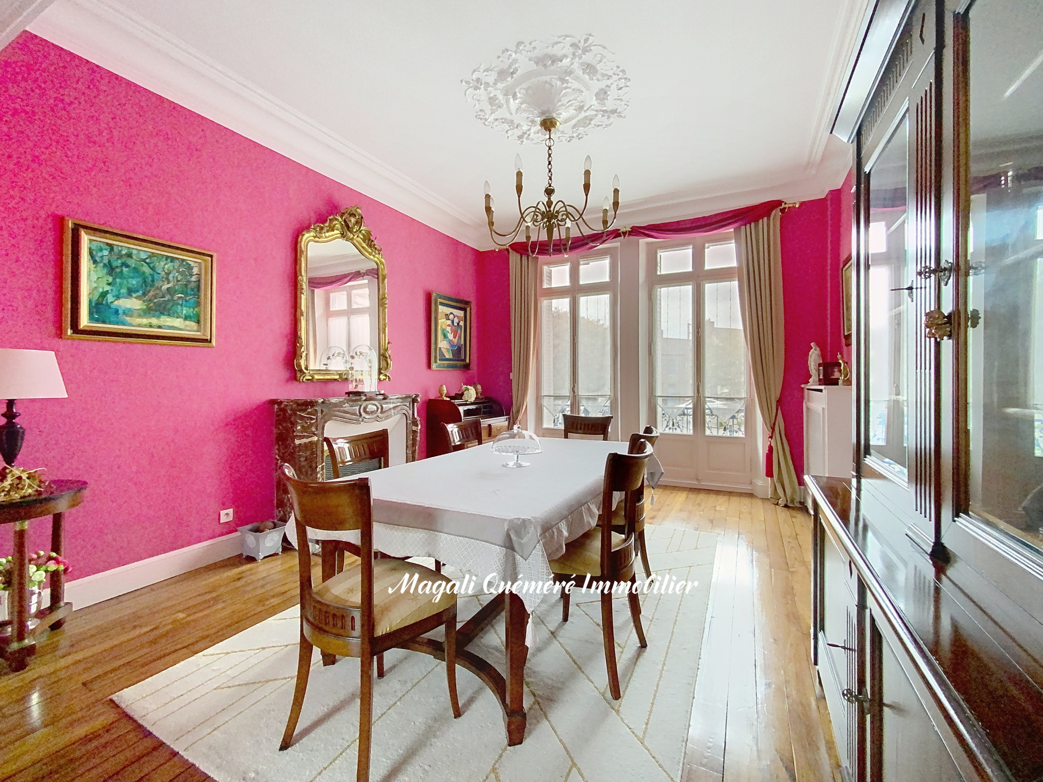 Elegant dining room with pink walls, a long white-covered table, and dark wooden chairs under a chandelier.