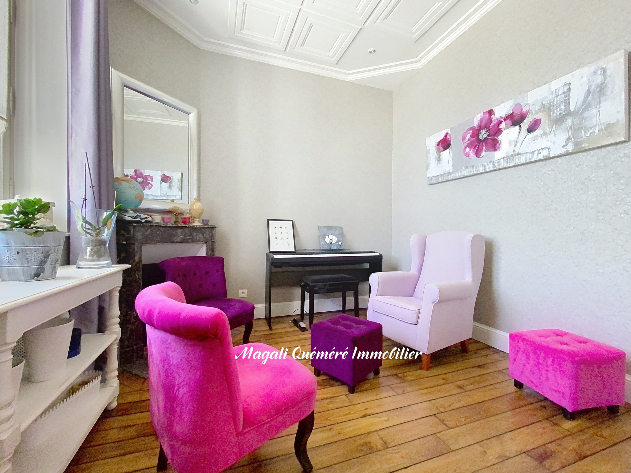 Cozy living room with pink velvet chairs and matching ottomans around a black piano, a lavender armchair, and a large pink-flower painting on a light wall.