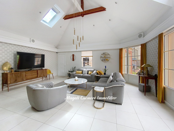 Bright, spacious living room with vaulted white ceiling, skylight, and gold pendant lights over a round coffee table area.