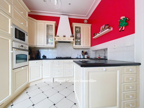Cream kitchen with beige cabinets, black countertops, gas stove, and double ovens against a red accent wall.