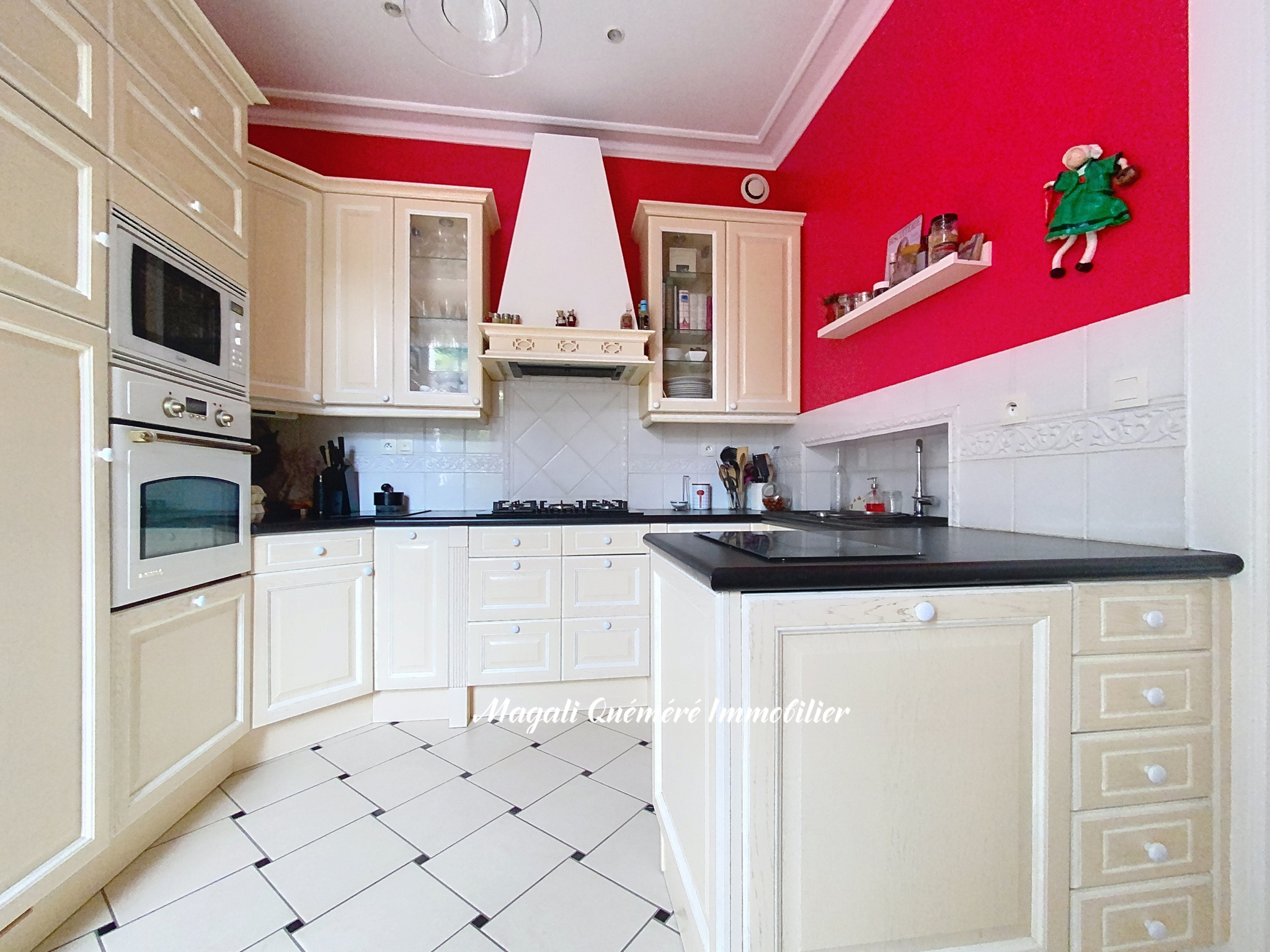 Cream kitchen with beige cabinets, black countertops, gas stove, and double ovens against a red accent wall.