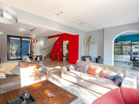 Spacious living room with beige sofas, colorful cushions, and a bold red geometric archway separating the space from the dining area.