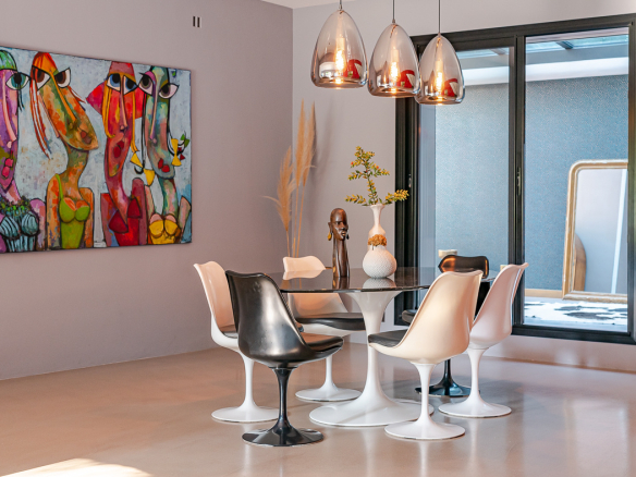 Modern dining area with a round glass table and white and black tulip chairs, and a vibrant abstract painting on the wall.