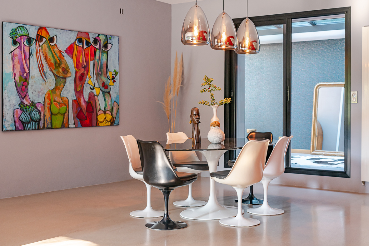 Modern dining area with a round glass table and white and black tulip chairs, and a vibrant abstract painting on the wall.