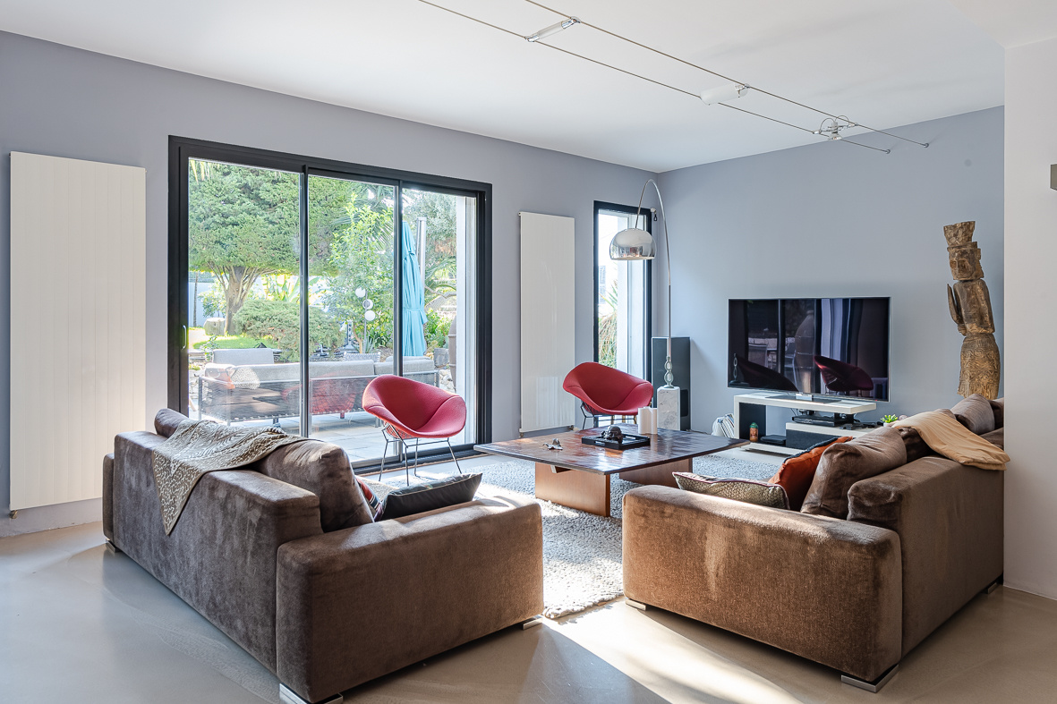 Bright modern living room with brown sofas, a wooden coffee table, and red accent chairs by large glass doors to the garden.