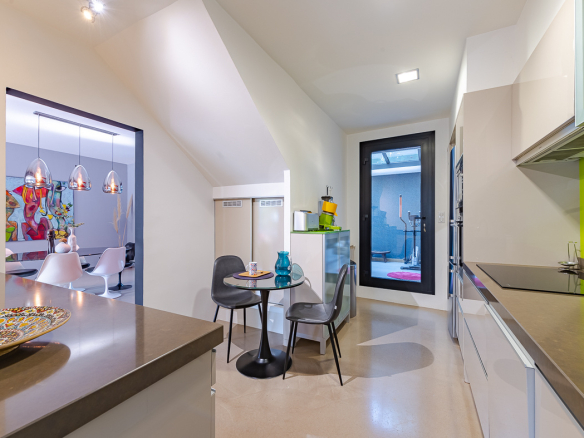 Open-plan kitchen with stainless counters, lime-green backsplash, a round glass table and two gray chairs.