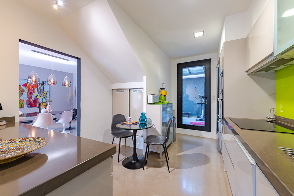 Open-plan kitchen with stainless counters, lime-green backsplash, a round glass table and two gray chairs.