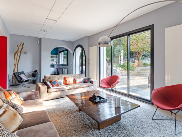 Bright modern living room with beigeSectional sofas, colorful cushions, and large sliding glass doors opening to a sunny patio.