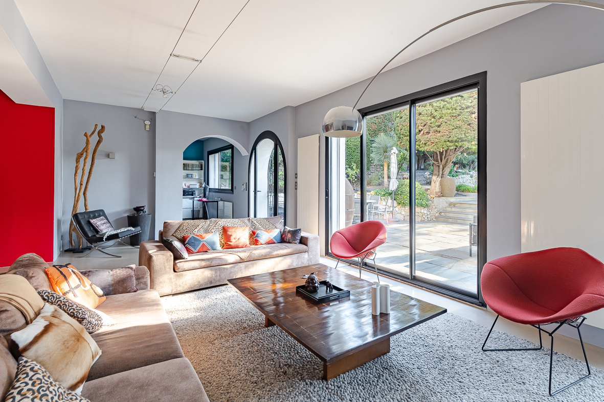Bright modern living room with beigeSectional sofas, colorful cushions, and large sliding glass doors opening to a sunny patio.