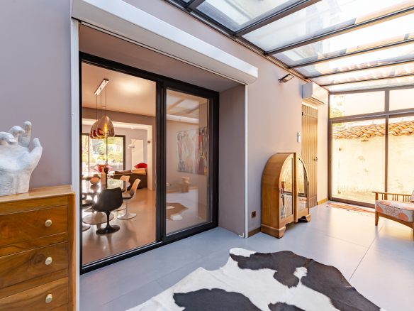 Sunlit indoor–outdoor living space with glass sliding doors, cowhide rug, and mid-century furniture pieces including a wooden dresser and vintage cabinet.