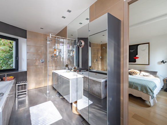 Luxurious bathroom with glass shower enclosure, freestanding tub, and a wide mirror wall; bedroom visible through the doorway.