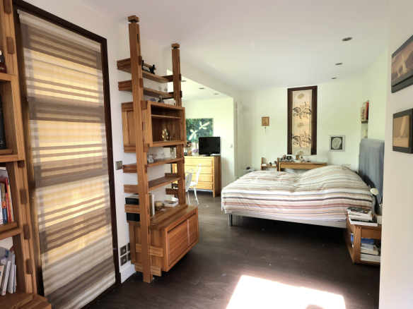 Bright bedroom with wooden modular shelves acting as a room divider, a striped bed with headboard, and a dresser with a small TV in the background.