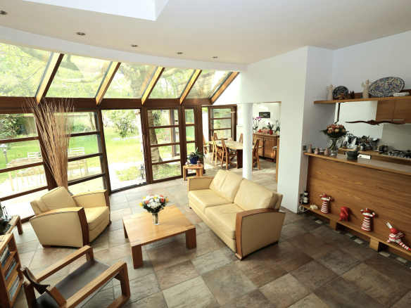 Bright open living room with beige sofas, wooden furniture, and large glass doors opening to a green garden outside.