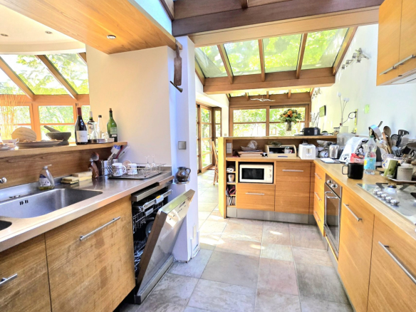 Bright kitchen with exposed wooden beams, large glass skylights, and L-shaped wooden cabinets with a stainless steel sink.