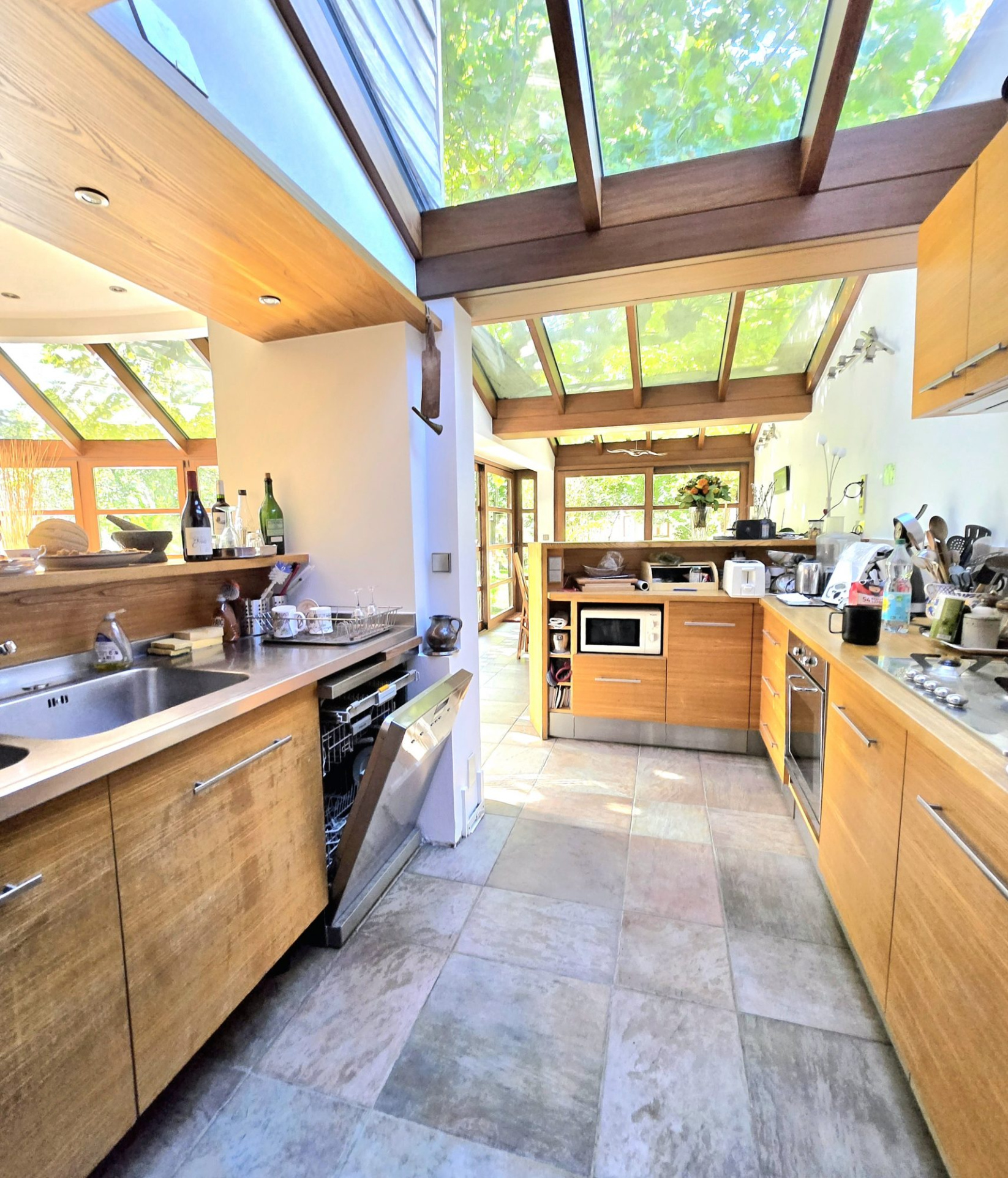 Bright kitchen with exposed wooden beams, large glass skylights, and L-shaped wooden cabinets with a stainless steel sink.