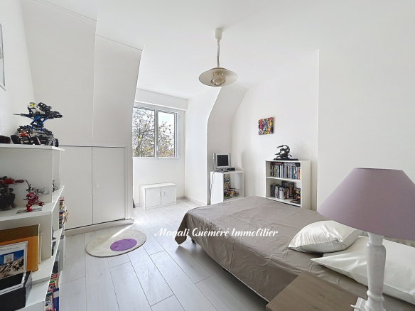 Bright white bedroom with a low bed, purple lamp, and white shelves full of toys and books, near a window showing trees outside.