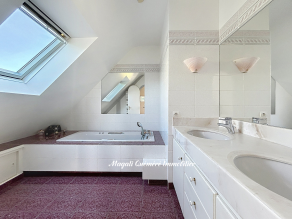 Bright attic bathroom with a corner bathtub, skylight, and a double-sink vanity reflecting in a mirror.