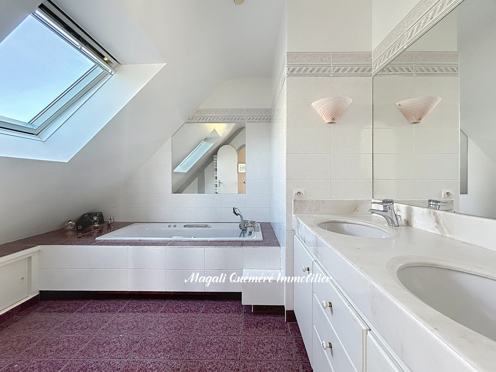 Bright attic bathroom with a corner bathtub, skylight, and a double-sink vanity reflecting in a mirror.