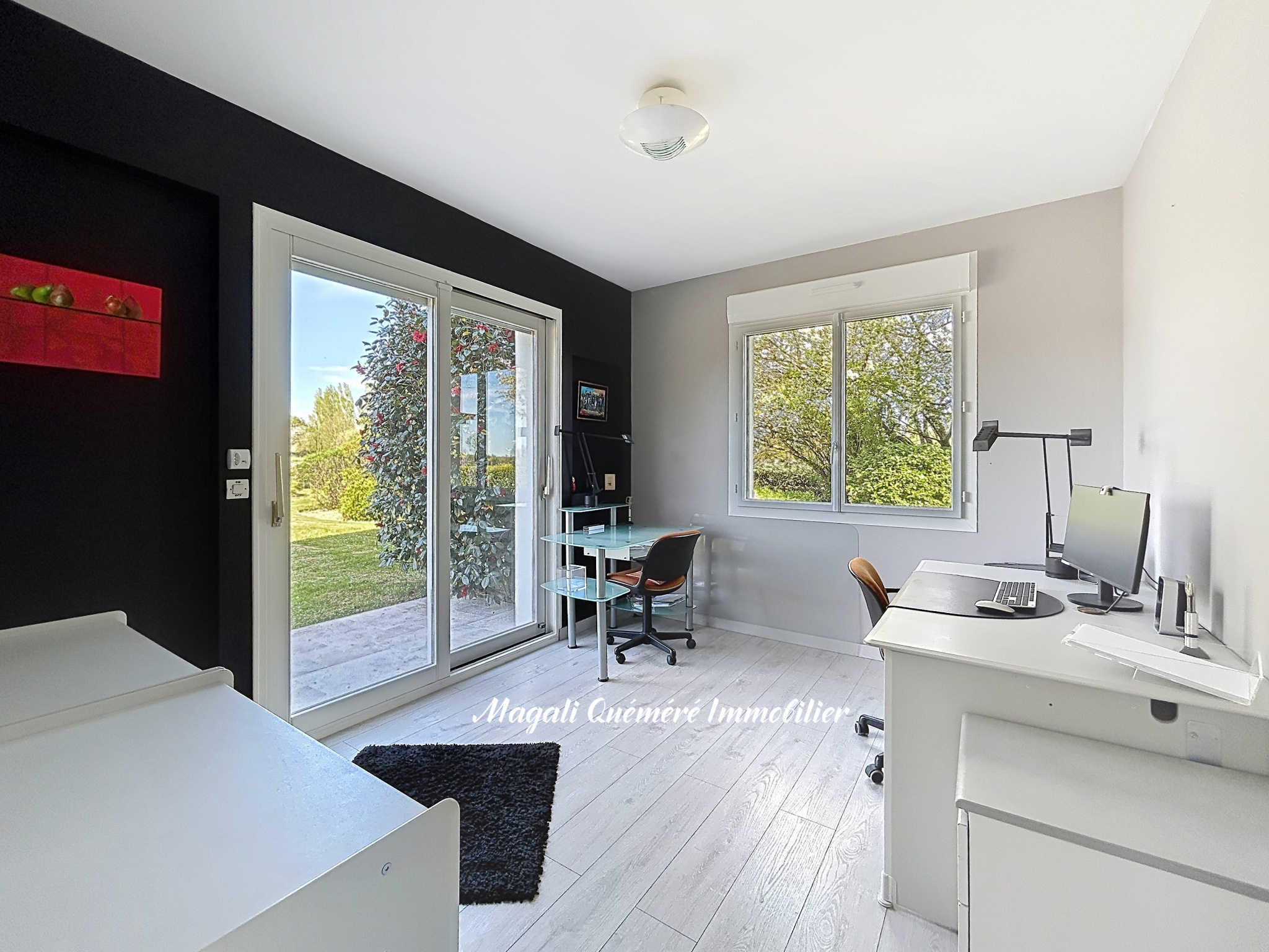 Minimalist home office: white desk, computer, chair, and a black accent wall with a sliding glass door to a garden outside.