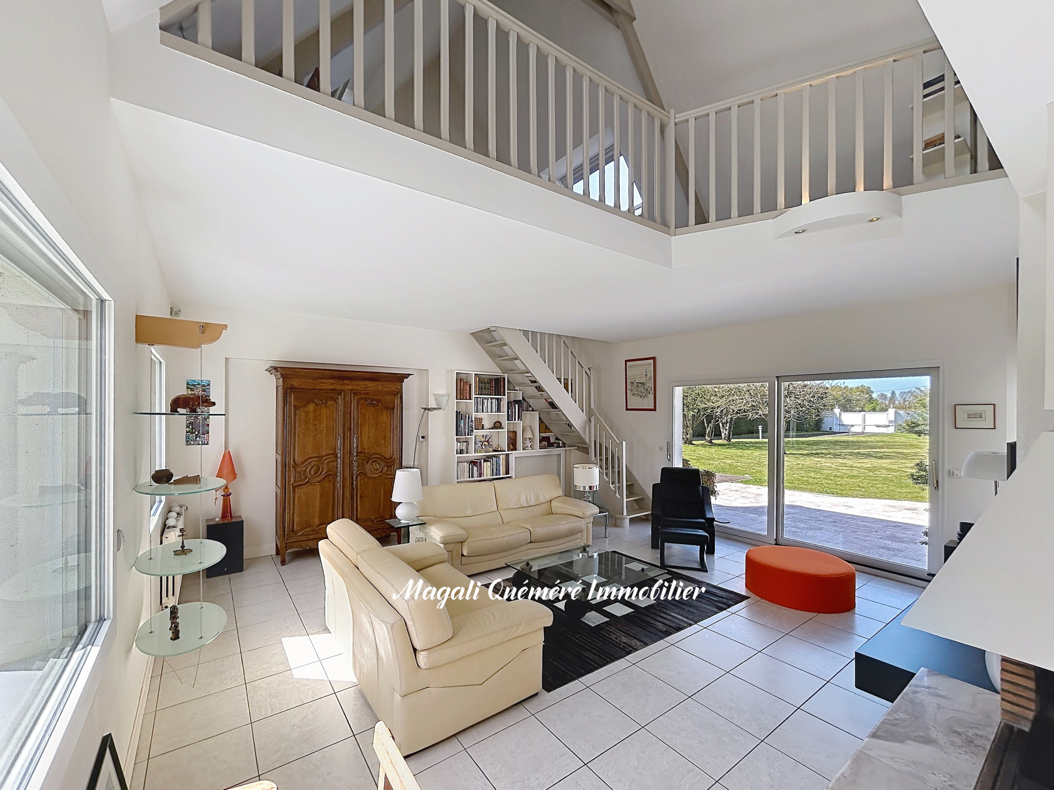 Bright open-plan living room with beige leather sofas, glass coffee table, and a white mezzanine above.
