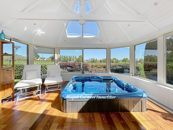 Bright glass conservatory with a blue hot tub, white lounge chairs, and a wooden floor overlooking a green garden in the yard.