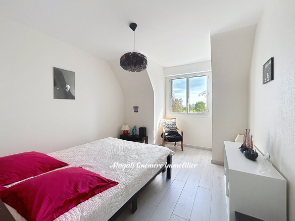 Bright minimalist bedroom with white walls, a bed with white quilt and two magenta pillows, and a black pendant lamp.