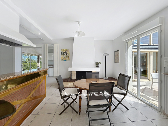 Bright open-plan living and dining area with a white fireplace, round wooden table, and four black chairs; sliding doors to an outdoor patio on the right.