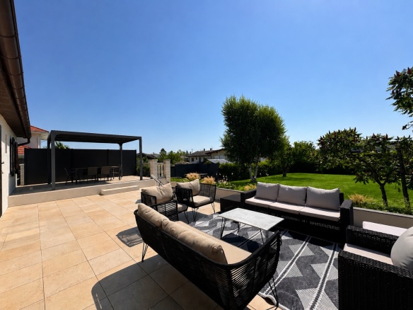 Sunny terrace with garden furniture and a view of a green garden in Saint-Genis-Pouilly.