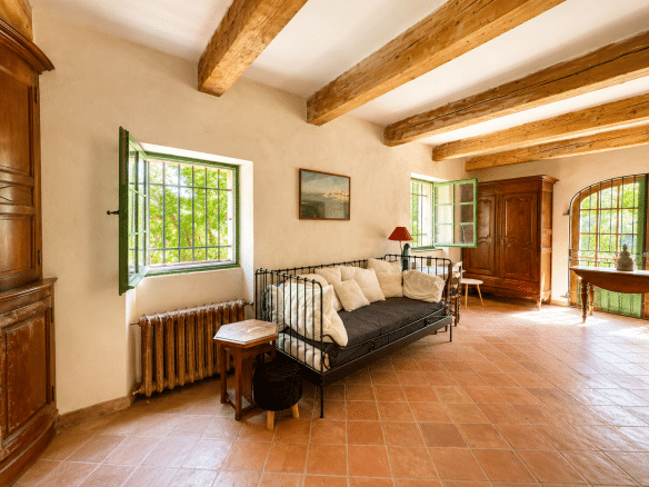 Intérieur d'un mas provençal avec canapé, fenêtres vertes et poutres en bois à Aubagne.