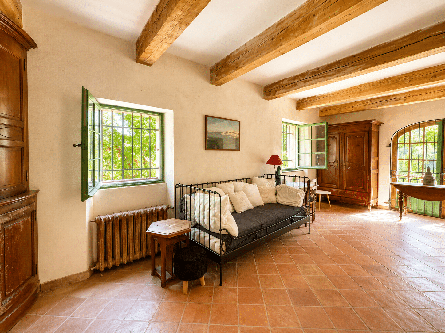 Intérieur d'un mas provençal avec canapé, fenêtres vertes et poutres en bois à Aubagne.