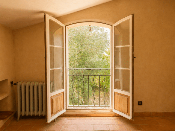 Intérieur d'une chambre avec fenêtres à double battant ouvrant sur un paysage verdoyant.