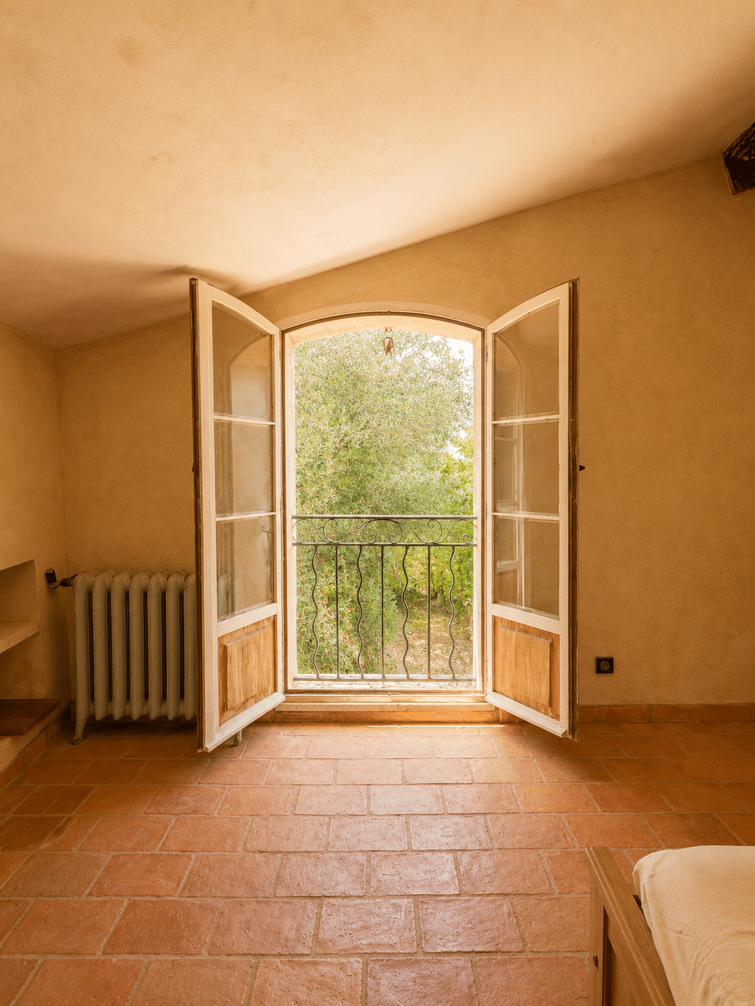 Intérieur d'une chambre avec fenêtres à double battant ouvrant sur un paysage verdoyant.