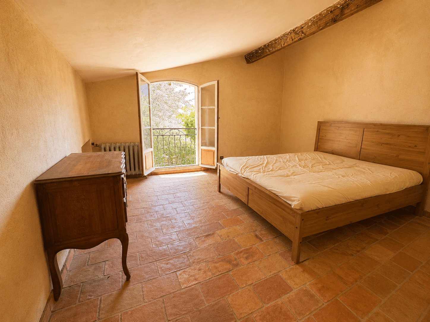 Chambre d'un mas provençal avec un lit en bois et une vue sur l'extérieur à Aubagne.