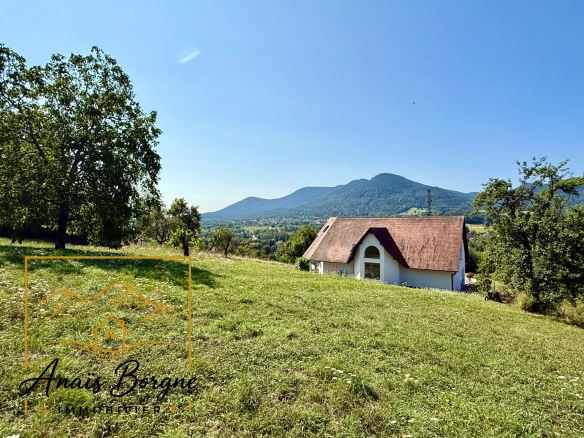 Villa avec toit en chaume sur un terrain verdoyant, vue sur la vallée et les montagnes environnantes.