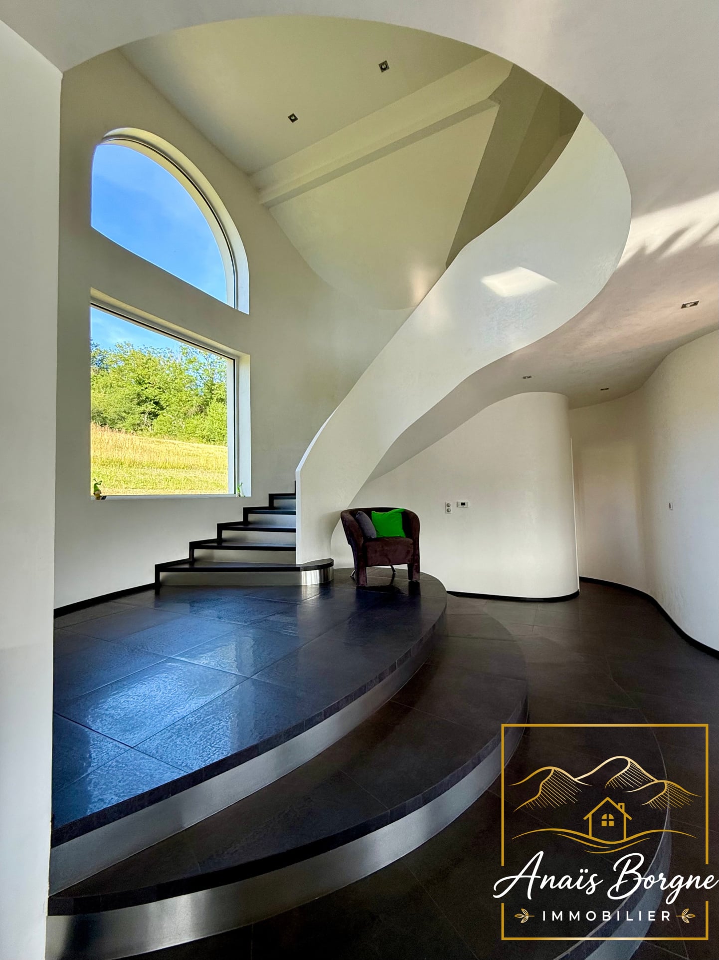 Intérieur d'une villa moderne avec un escalier en colimaçon et une grande fenêtre.