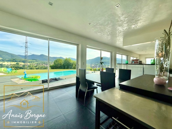 Intérieur d'une villa moderne avec vue sur la vallée, piscine et montagnes en arrière-plan.