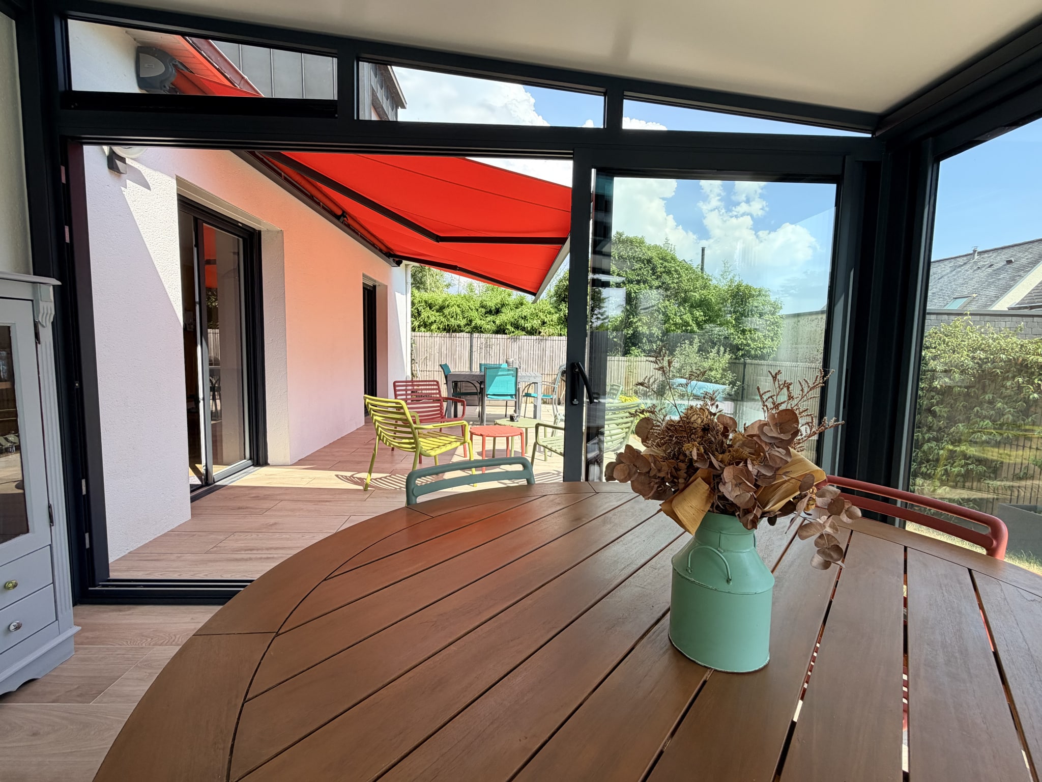 Véranda lumineuse d'une maison contemporaine à Vannes, avec mobilier coloré et vue sur l'extérieur.