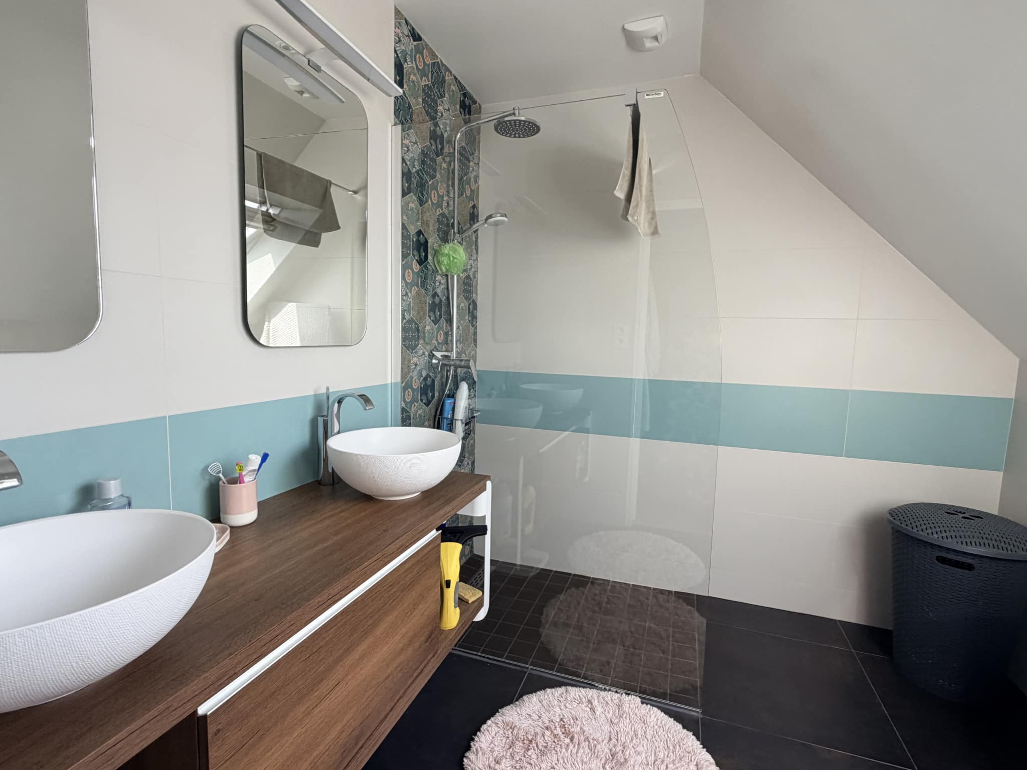 Salle de bain moderne avec douche, lavabos sur meuble en bois et carrelage contemporain.