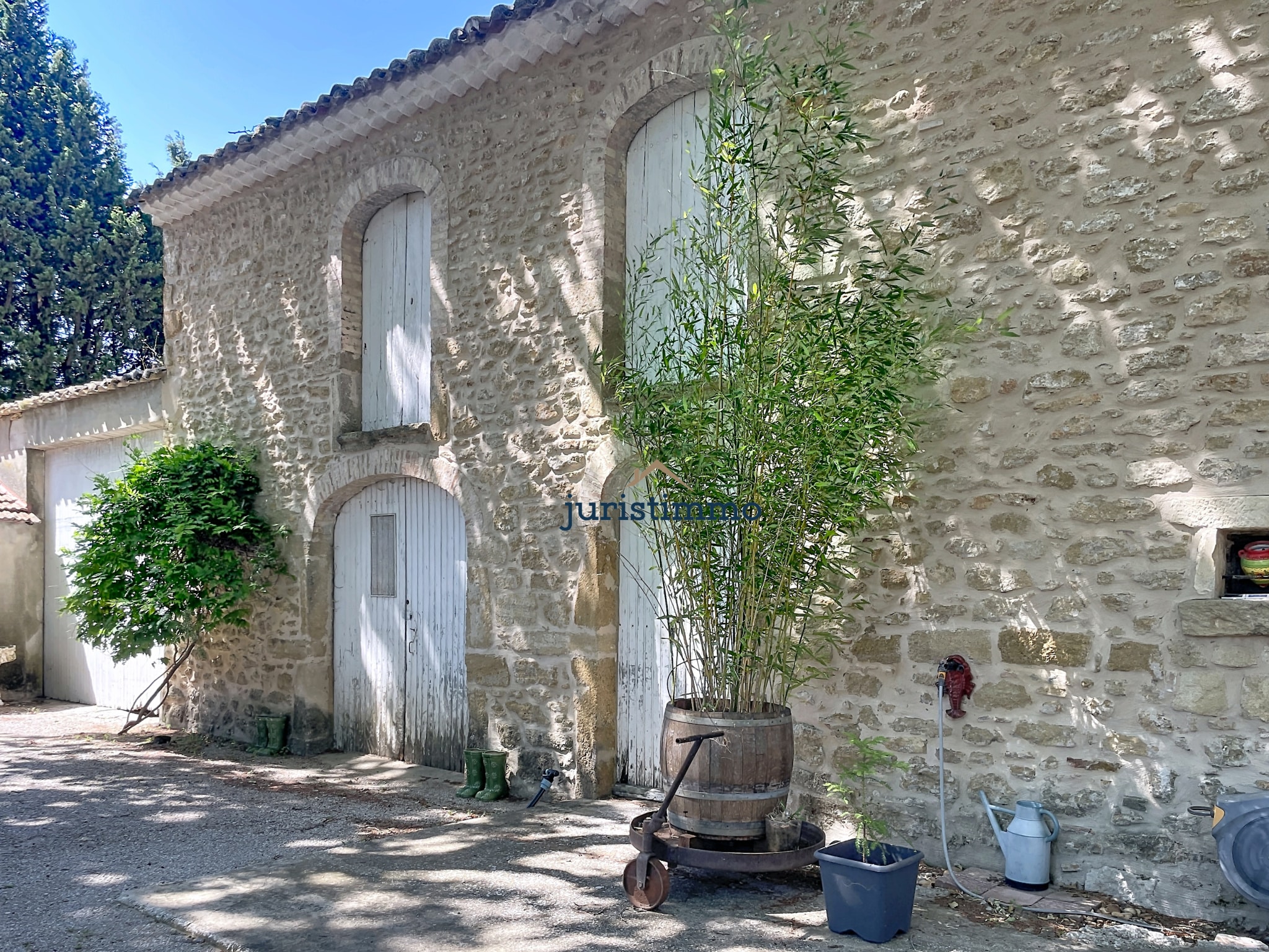 Bâtiment en pierre avec des volets blancs, entouré de verdure, dans un parc arboré.